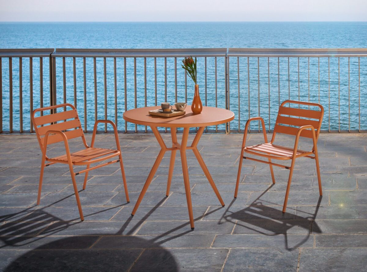 Ein orangefarbenes Bistroset auf einer weitläufigen Terrasse, im Hintergrund Wasser.