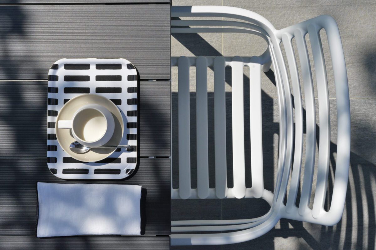 Blick von oben auf einen weißen Gartenstuhl an einem dunklen Tisch.