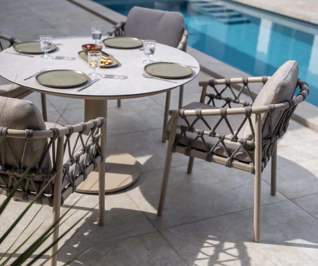 Runder Tisch mit Rope-Sesseln stehen neben einem blauen Pool