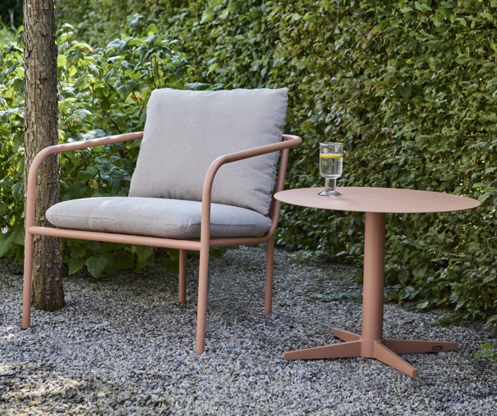 Loungesessel mit Kissen und Beistelltisch vor einer Hecke