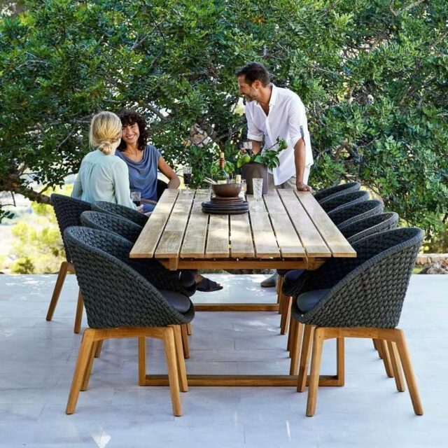 Ein Mann und zwei Frauen an einem langen Teakholztisch mit gemütlichen Schalensesseln aus Soft Rope mit Teakholzbeinen