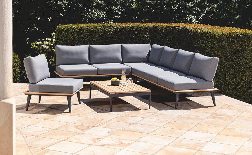 Gemütliche Ecklounge mit Holz-Elementen auf einer sonnigen Terrasse vor einer Hecke