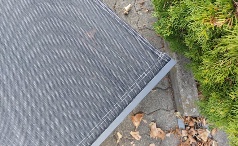 Detail einer Gartenliege mit grauem Textilen. Auf dem Terrassenboden liegt Herbstlaub