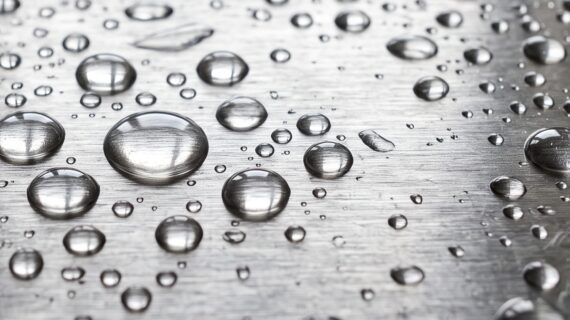 Abperlende Wassertropfen auf gebürstetem Edelstahl (KI-generiert)